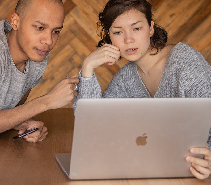 A couple intently watches a video on a laptop.